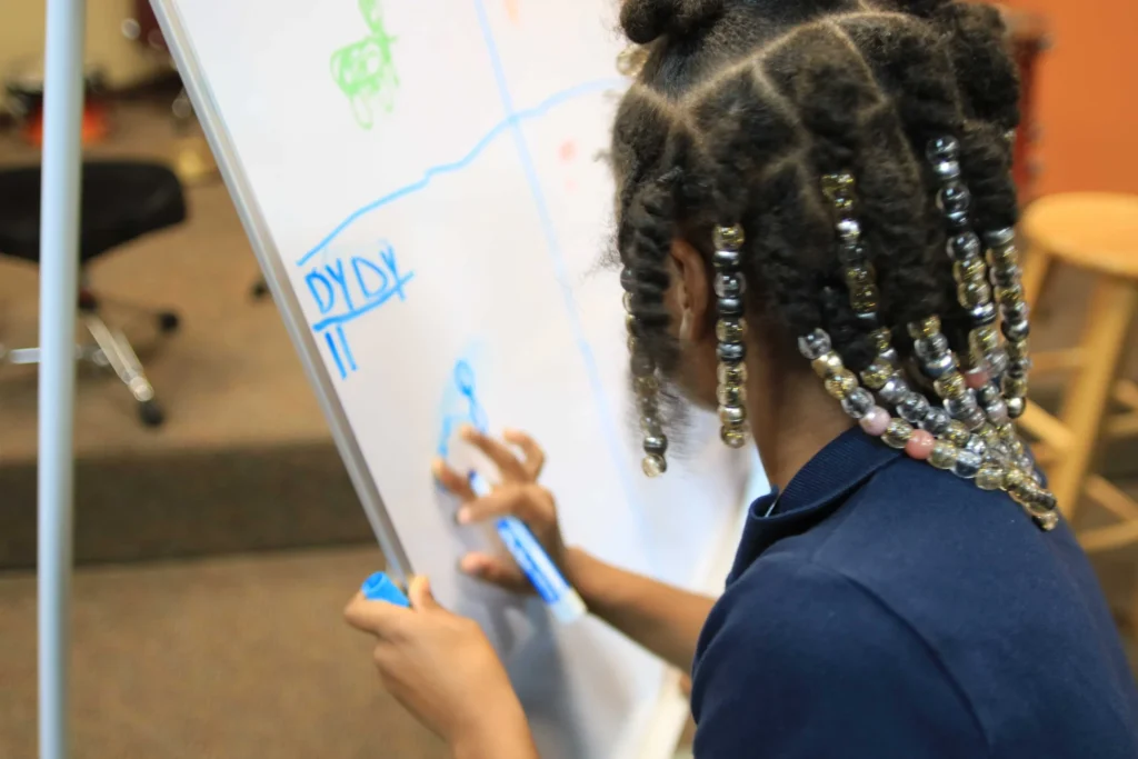 A child practising mathematics at a whiteboard at Reed’s Refuge