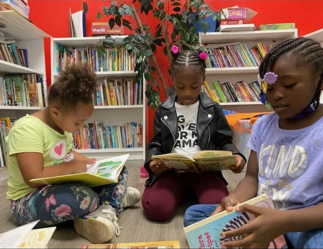 Three children reading books together in the Reed’s Refuge library